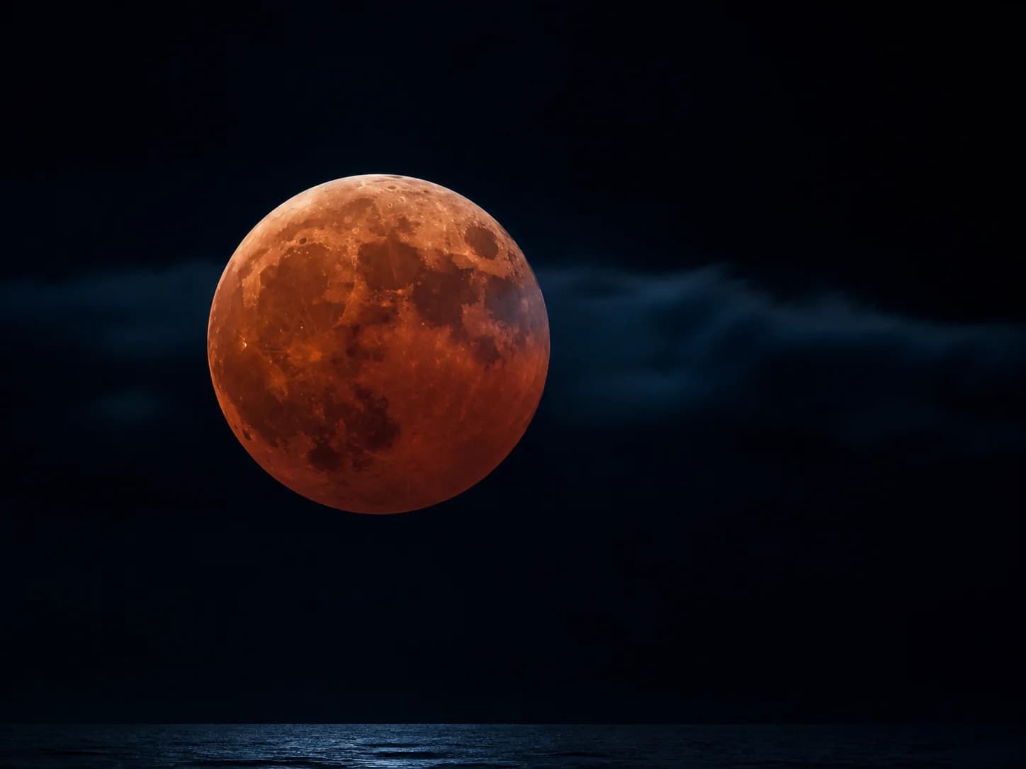 Copper-red Moon over a silhouetted British observatory during totality